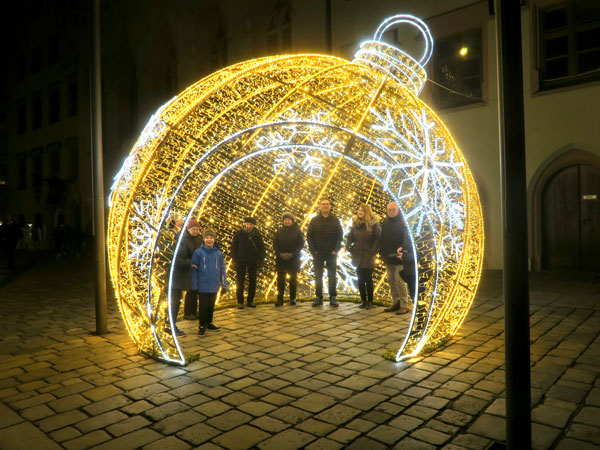 Goldfarben erleuchtete Kuppel in Form einer Weihnachtskugel, ca. 5 Meter hoch, steht auf dem gepflasterten Platz vor dem Landshuter Rathaus. Sie ist begehbar, hat einen hohen, bogenförmigen Eingang und drinnen stehen 8 Damen und Herren.